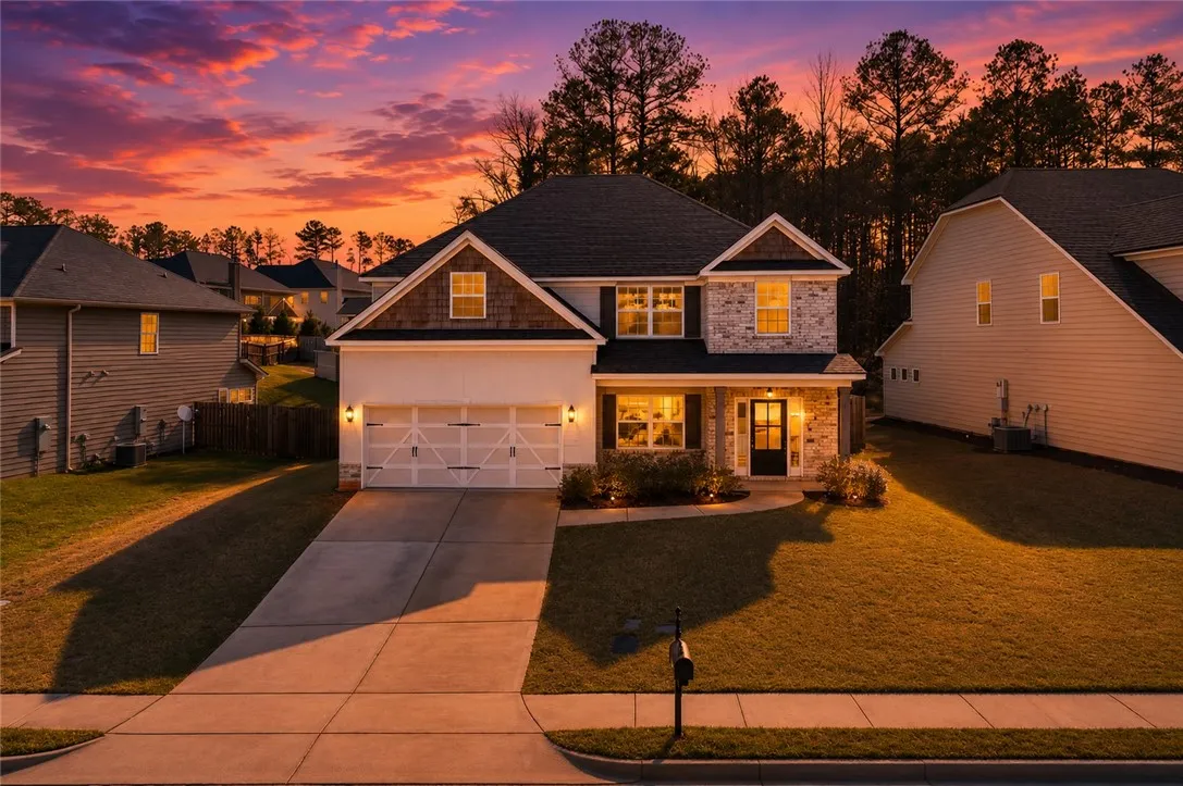 Twilight glows over a welcoming residence featuring a dual-door garage and a neatly maintained front lawn.