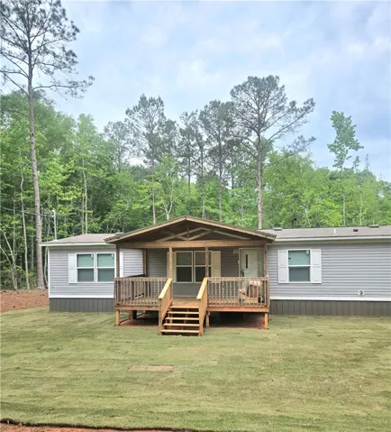 This charming home features a welcoming porch set against a lush, wooded backdrop.