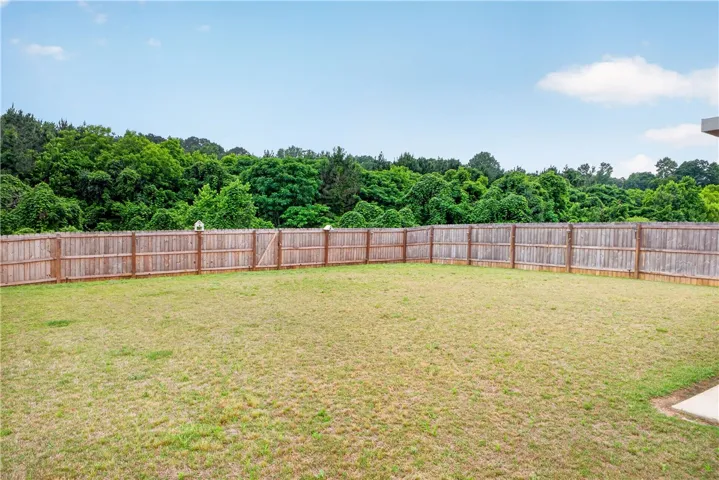 A spacious, enclosed backyard offers ample green space and a natural tree-lined perimeter.