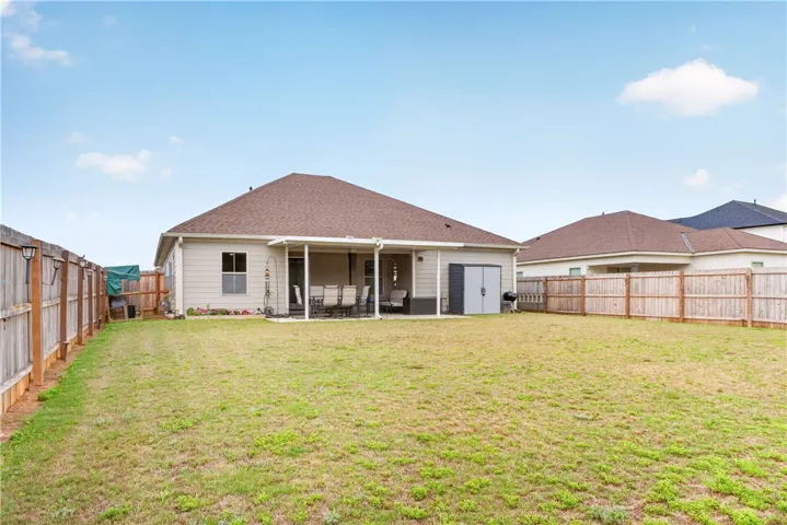 An inviting covered patio opens to a spacious backyard, fully enclosed by fencing.