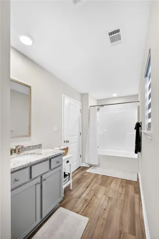 Modern bath with granite counters, sleek LVP flooring, and a pristine shower-tub combination.