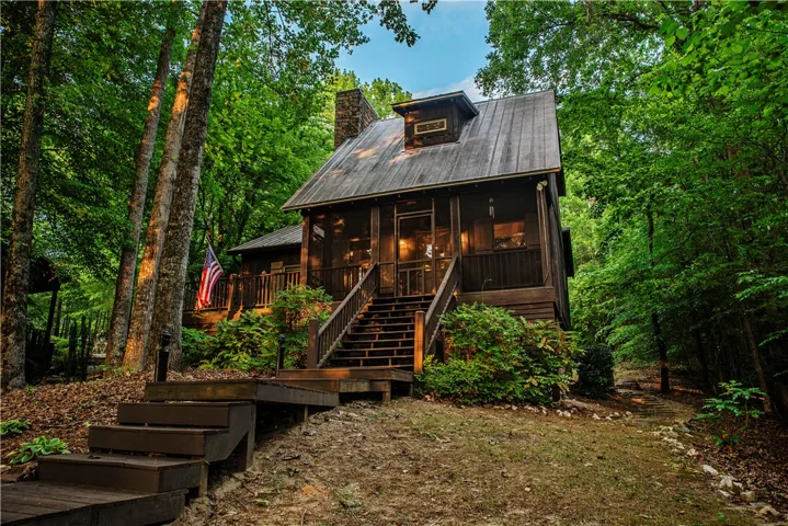 This secluded forest retreat features a charming cabin with a welcoming screened porch and rustic wood siding.