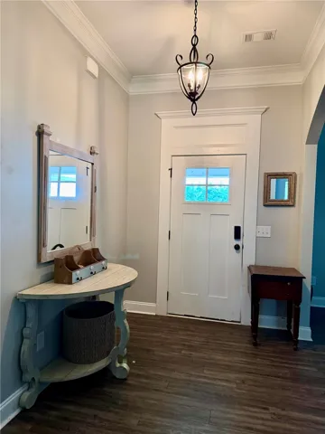 A welcoming entryway with rich wood-toned flooring and elegant crown molding sets an inviting tone.