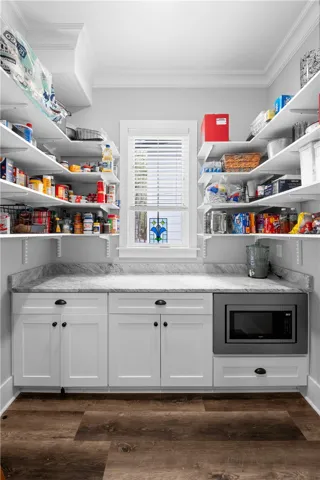 A truly exceptional pantry with a built-in microwave, custom cabinetry, open shelving, marble countertops, and natural light from a well-placed window.
