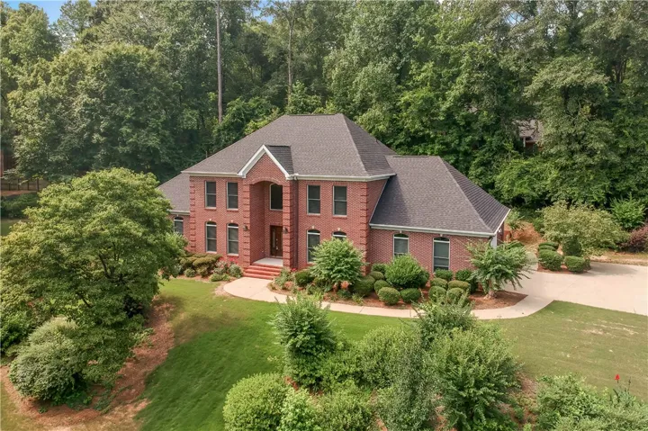 Grand brick facade nestled amidst verdant landscaping and mature trees, offering a private setting.