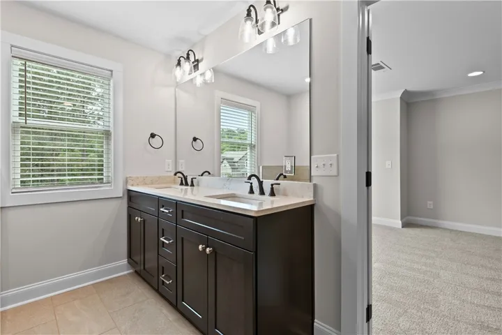 This angle of the primary bathroom offers ample vanity space and pristine tile flooring.
