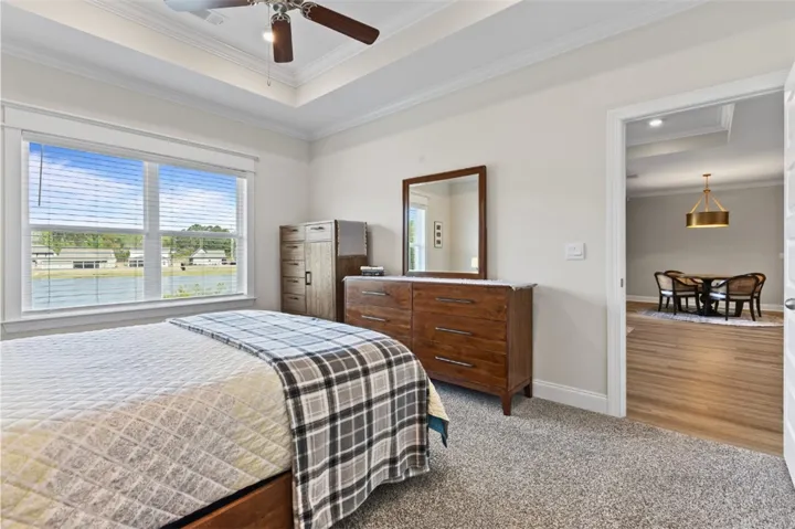 Primary bedroom w/ crown molding overlooking fenced backyard with a lake view