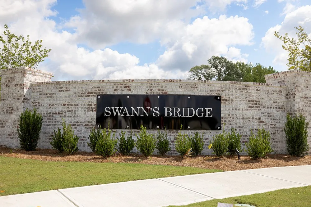 This grand entrance features a brick wall, lush landscaping, and a welcoming community sign.