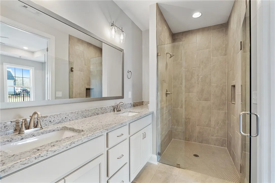 This spacious bathroom features a walk-in shower and a double vanity with ample counter space. Photos are not of subject property. Photos are of the same floorplan of a completed home.