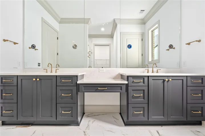 The primary bath's extended vanity offers dual sinks and a dressing table. A zero-enty tiled shower is beyond.
