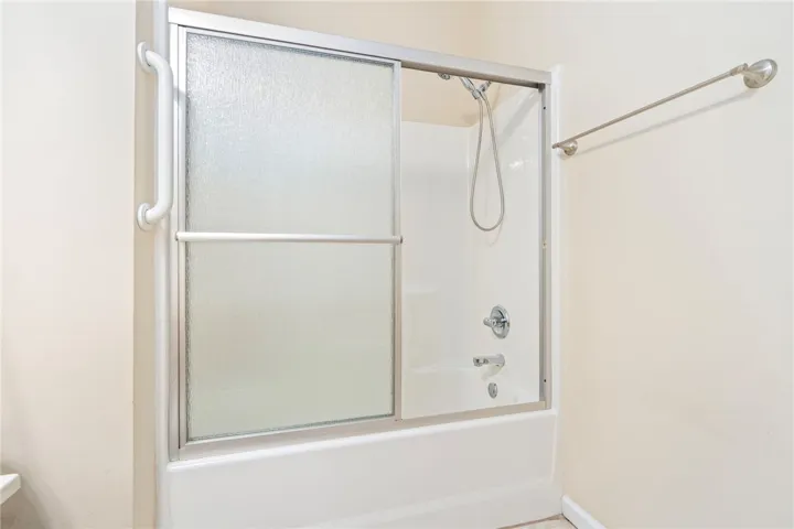 A well-maintained tub-shower combination features practical sliding glass doors and a convenient grab bar.