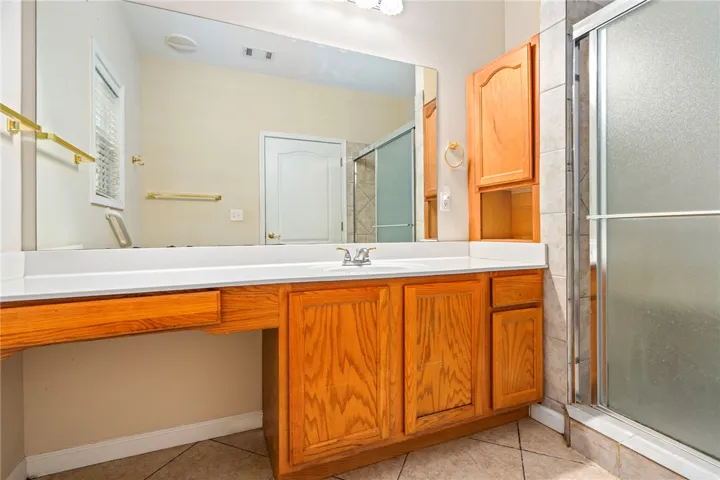 A practical Master bathroom vanity features ample counter space, integrated sink, and warm wood cabinetry, alongside a private shower stall.