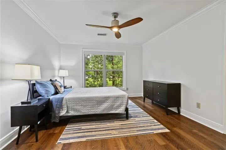 This serene primary bedroom offers warm wood flooring and a refreshing view of lush greenery through its large window.