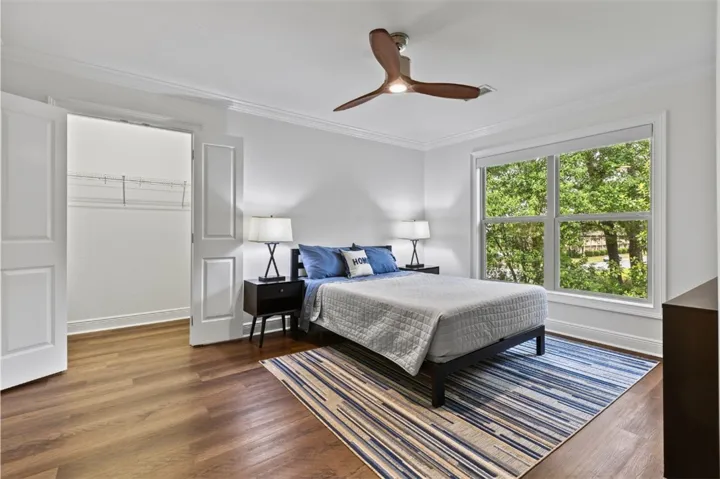 This inviting primary bedroom features rich wood flooring, a ceiling fan, and large windows that frame verdant outdoor views.