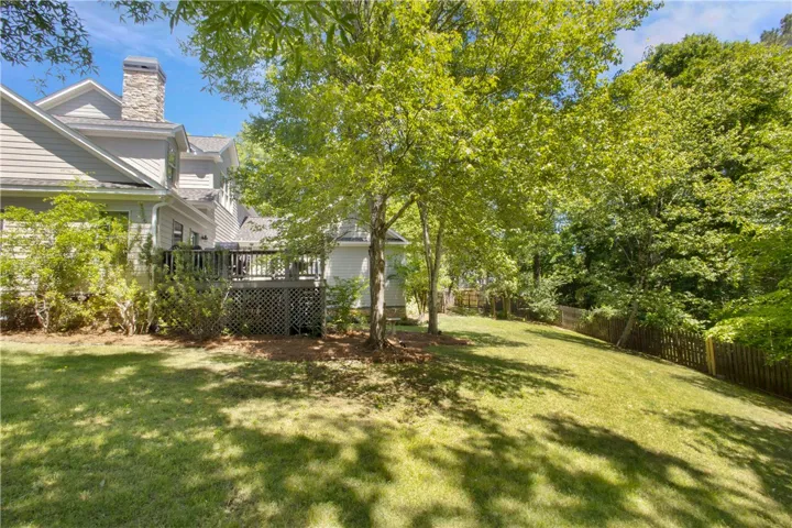 An inviting outdoor space features a spacious deck, perfect for gatherings amidst lush greenery and mature trees.