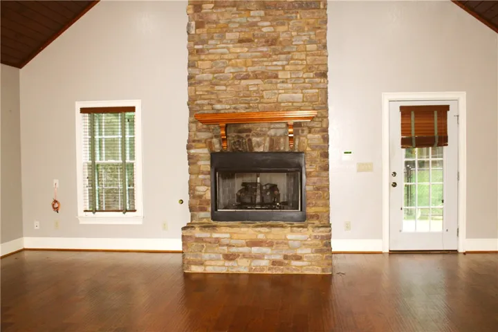 This inviting living space features a cozy stone fireplace, high ceilings, and rich hardwood flooring.