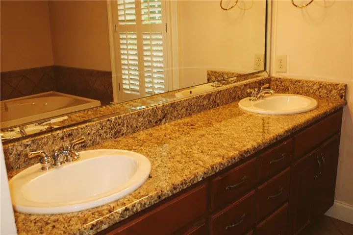 This primary bathroom offers dual sinks with stone counters and a spacious soaking tub.