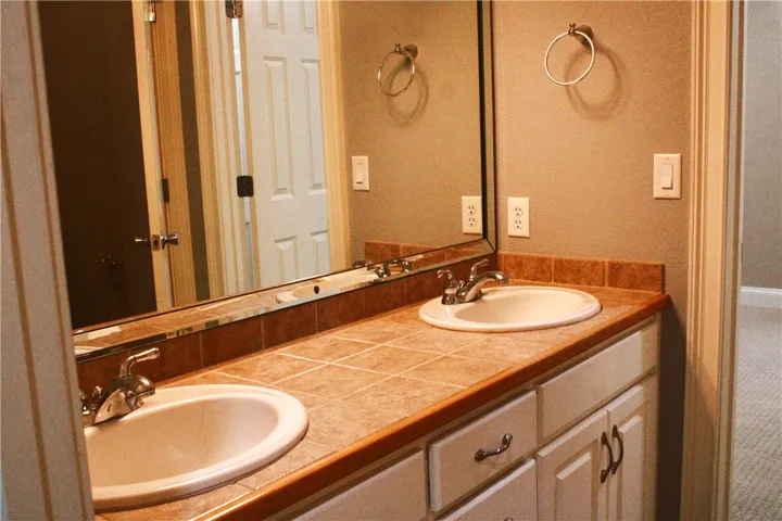 This bathroom features a double vanity with tile countertops and a large mirror.