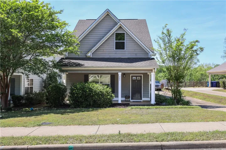 This charming home features a welcoming porch, lush landscaping, and a classic gabled roof design.
