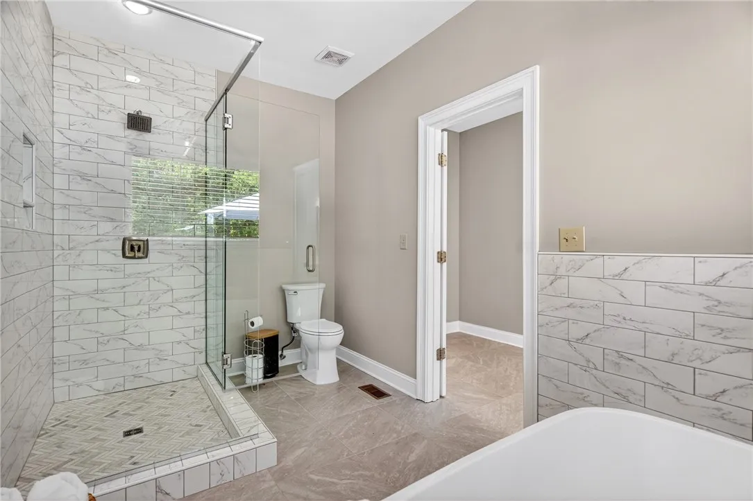 This bathroom features a sleek glass-enclosed shower, a pristine toilet, and durable tile flooring.