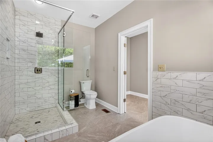 This bathroom features a sleek glass-enclosed shower, a pristine toilet, and durable tile flooring.