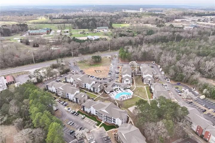 An aerial view showcases a residential complex nestled among lush greenery, featuring ample parking and a refreshing pool.