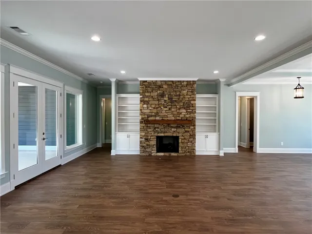 An inviting open-concept living area features a grand stone fireplace, built-in shelving, and warm wood flooring.