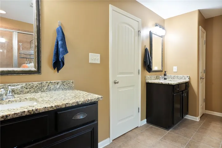 This bathroom offers dual vanities with elegant granite countertops and practical tile flooring.