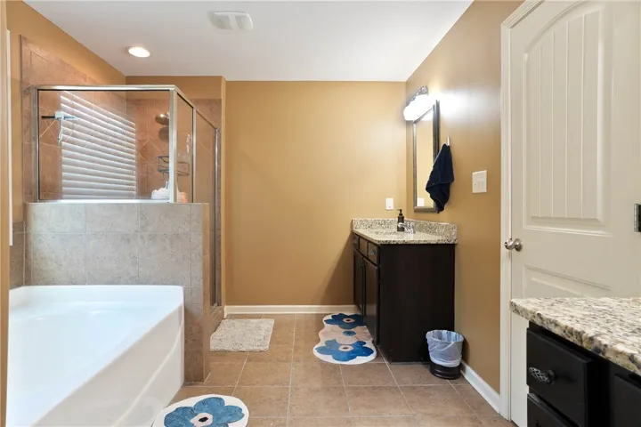 This primary bathroom features a shower, a soaking tub, and a vanity with a granite countertop.