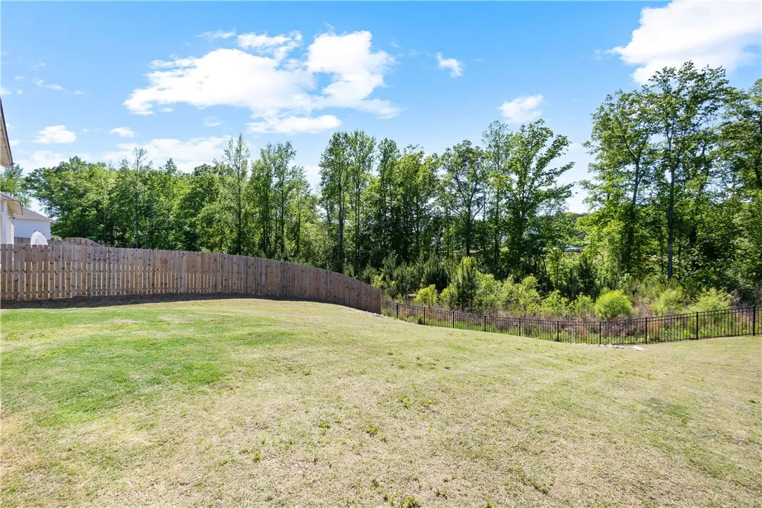 A spacious, grassy yard offers ample room for recreation, bordered by natural greenery and a secure fence.