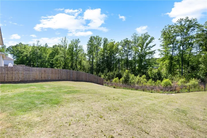 A spacious, grassy yard offers ample room for recreation, bordered by natural greenery and a secure fence.