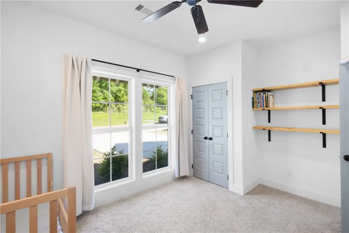 Bright windows frame green views in this serene, carpeted bedroom.
