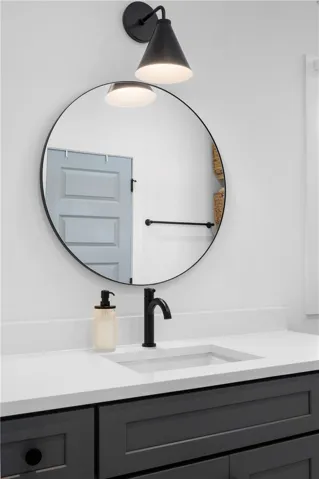 Modern bath vanity with sleek counters and a circular mirror, featuring a stylish black faucet.
