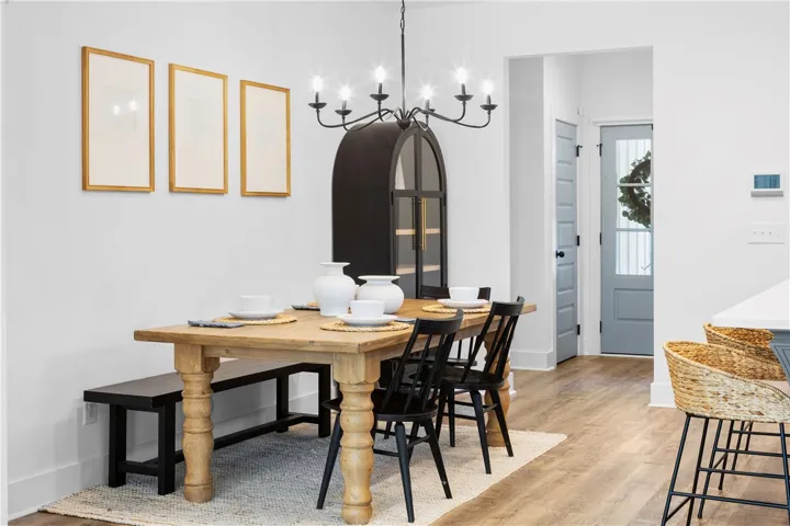A well-lit dining area featuring a light wood table, stylish dark chairs, and wood flooring.