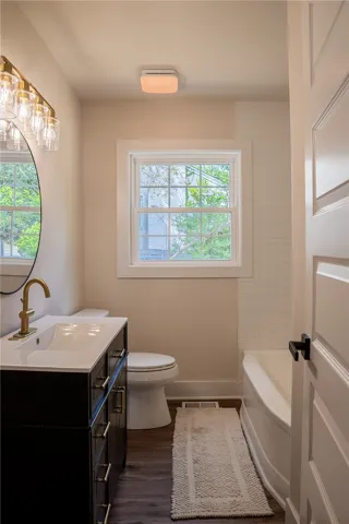 This bright bathroom features a vanity, window, and a bathtub with tiled walls.