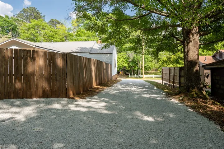 This property features a spacious gravel driveway leading to a fenced yard, shaded by mature trees.