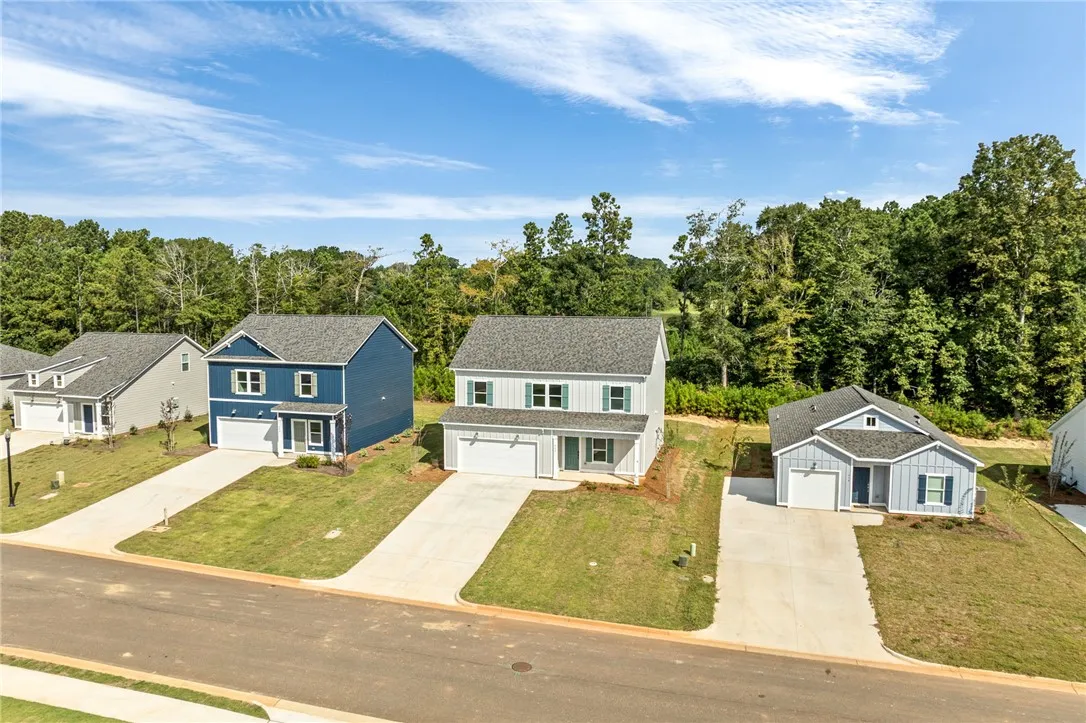 An aerial view showcases new construction homes with concrete driveways set against a dense forest backdrop.
