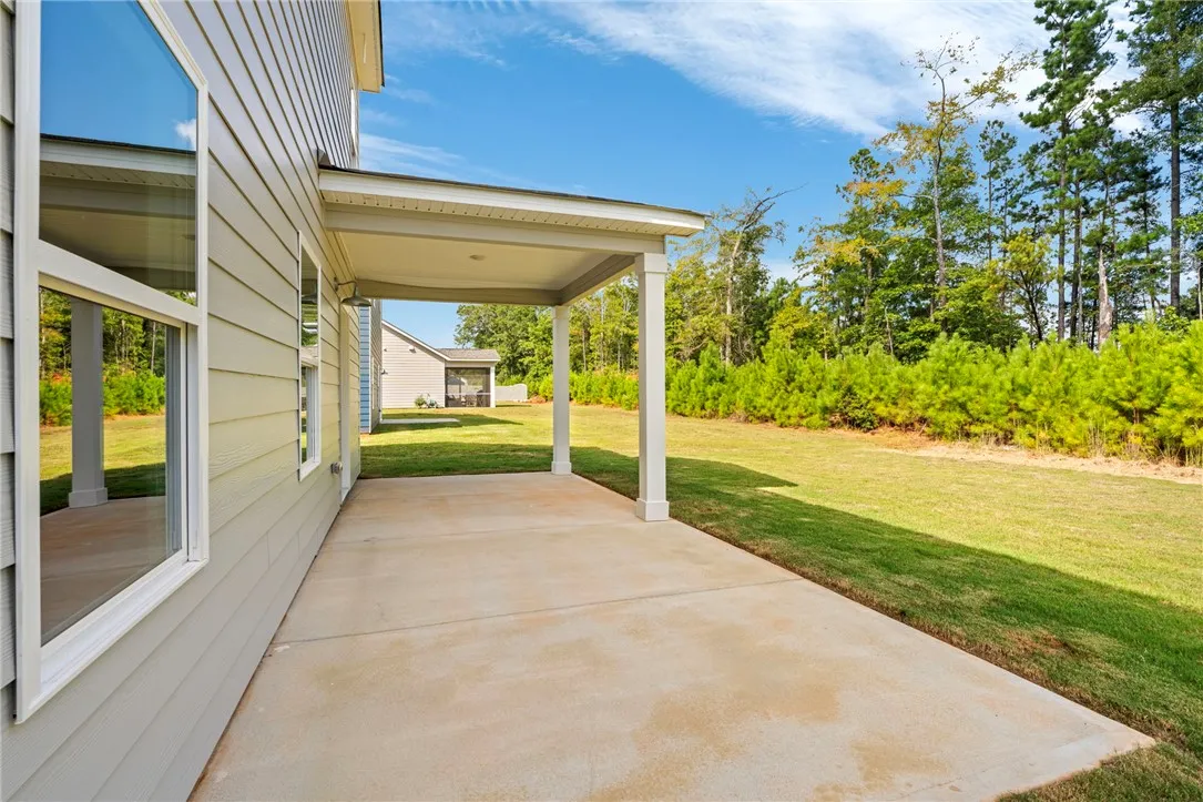 A covered concrete patio overlooks a grassy backyard bordered by mature trees.