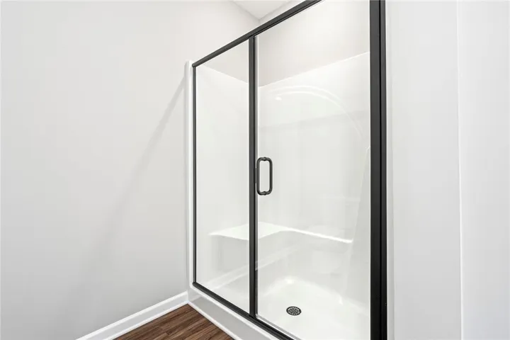 Rich wood-toned flooring contrasts beautifully with the clean lines of a modern walk-in shower.