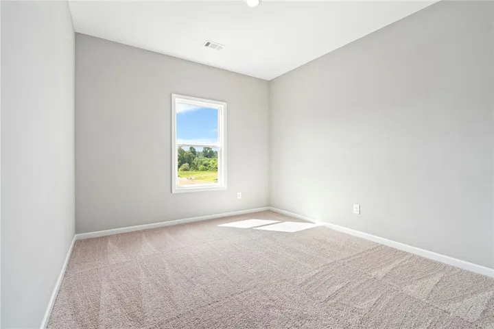 Plush carpeting and a single window overlooking green spaces define this quiet bedroom.