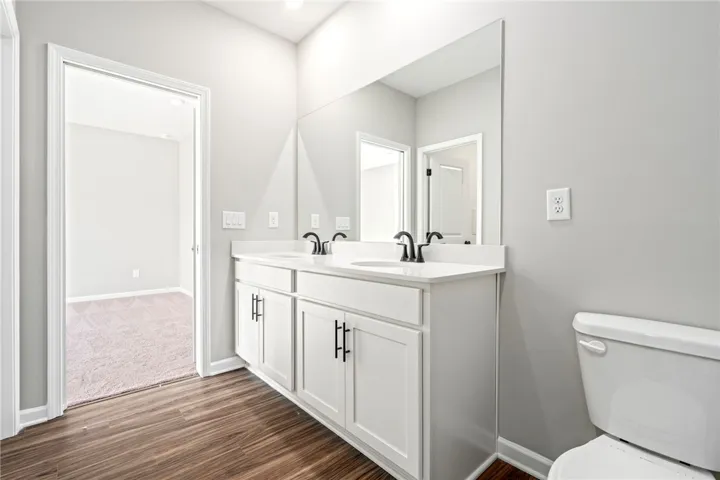 Clean lines and a spacious dual vanity define this modern bathroom with wood flooring.