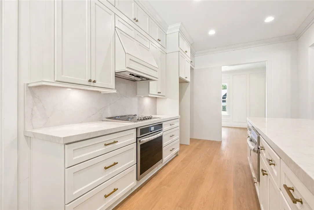 In the thoughtfully designed kitchen, the countertop slab continues seamlessly as the backsplash, creating a cohesive, elevated look, while the layout accommodates dual ovens and a gas range.