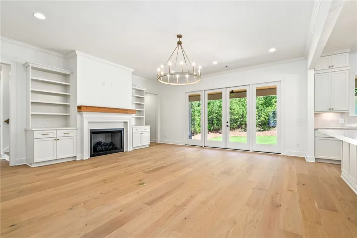 A full-light four-door system, a fireplace flanked by custom built-ins, and a central chandelier define the main gathering space.