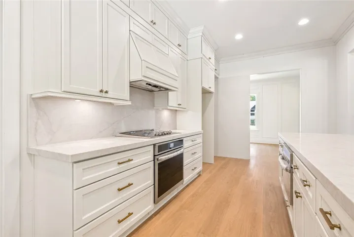 In the thoughtfully designed kitchen, the countertop slab continues seamlessly as the backsplash, creating a cohesive, elevated look, while the layout accommodates dual ovens and a gas range.