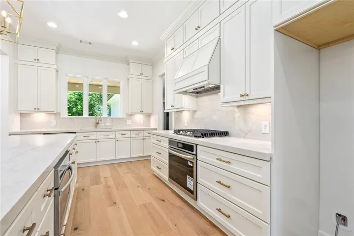 In the thoughtfully designed kitchen, the countertop slab continues seamlessly as the backsplash, creating a cohesive, elevated look, while the layout accommodates dual ovens and a gas range.
