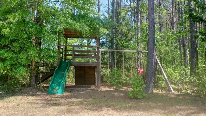 This playful outdoor area features a wooden playset, swings, and a slide, surrounded by lush trees.