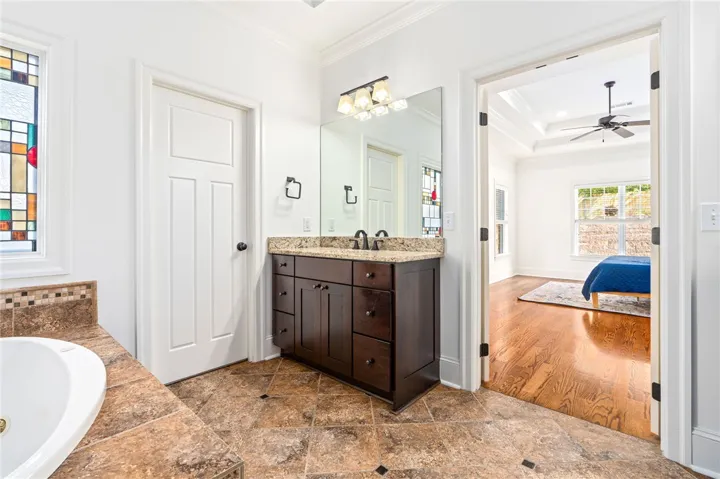 This spacious primary bathroom offers a double vanity and a built-in tub, with natural light from a decorative window.
