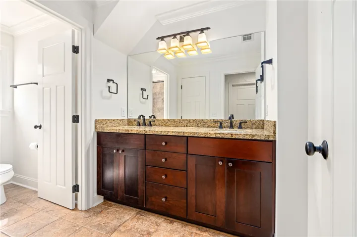 This bathroom features a double vanity with ample storage and elegant granite counters, a warm-toned tile surrounding the tub, creating a cozy and inviting space.