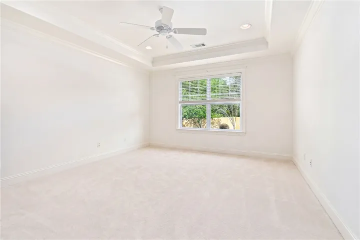 This spacious bedroom offers elegant tray ceilings, recessed lighting, and soft carpet flooring.