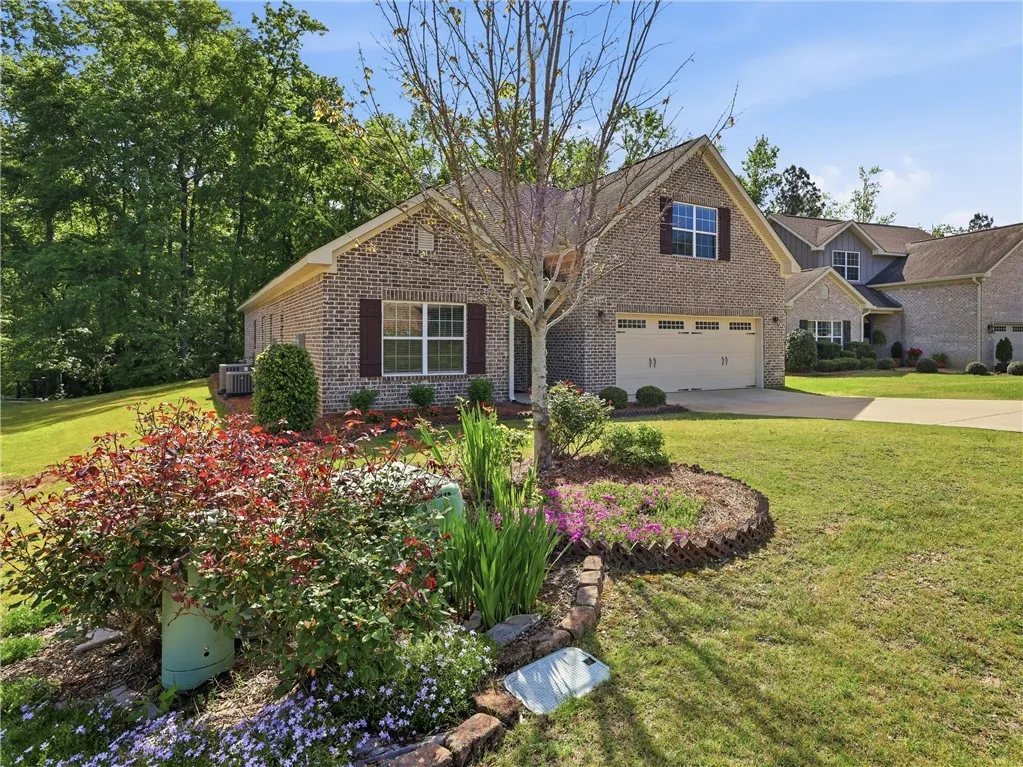 This charming brick home features an attached garage, a well-maintained lawn, and a beautiful garden.